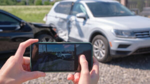 stressed driver taking picture on sellphone camera of smashed vehicle